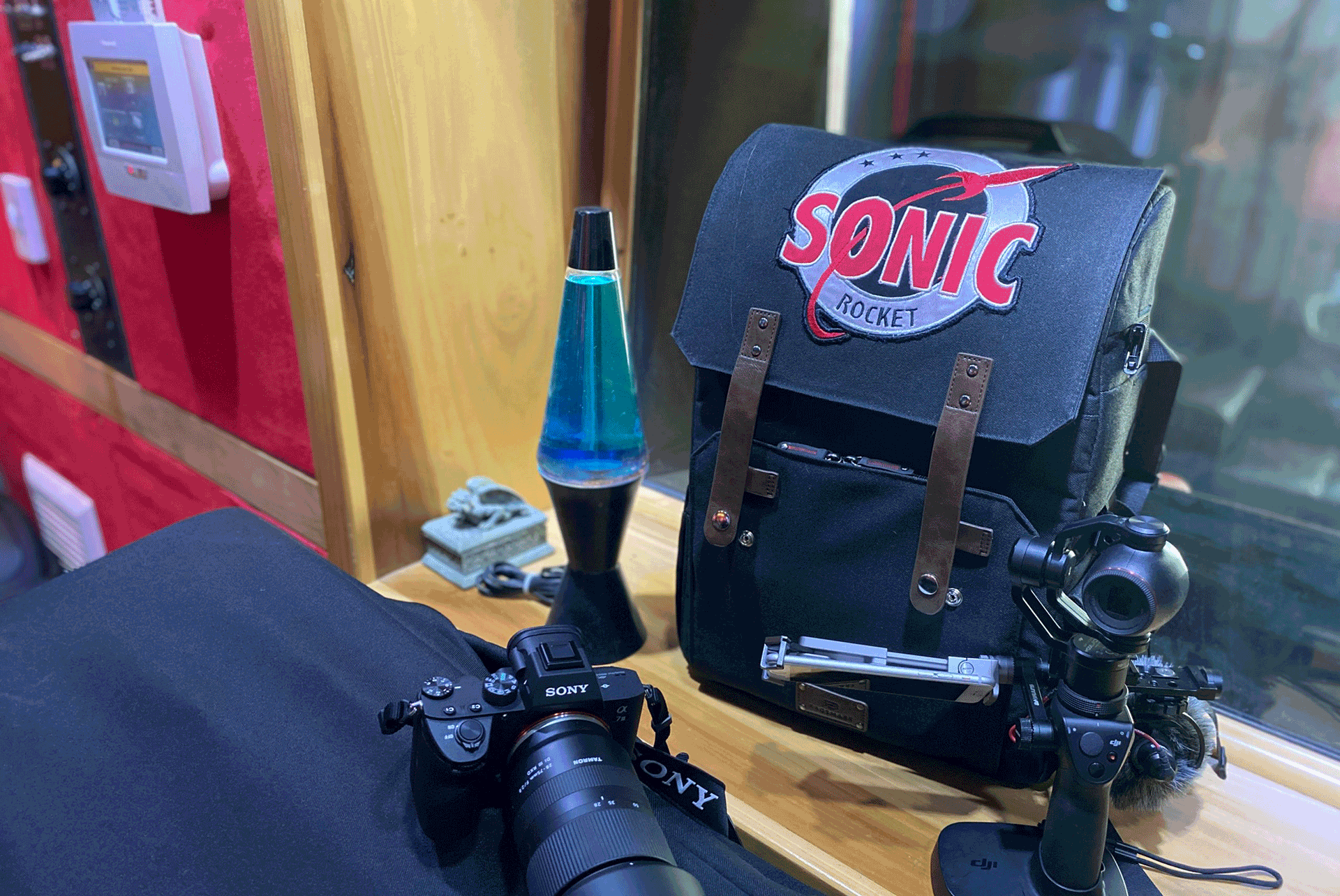 Sony camera with a lens placed next to a Sonic Rocket branded backpack on a surface.