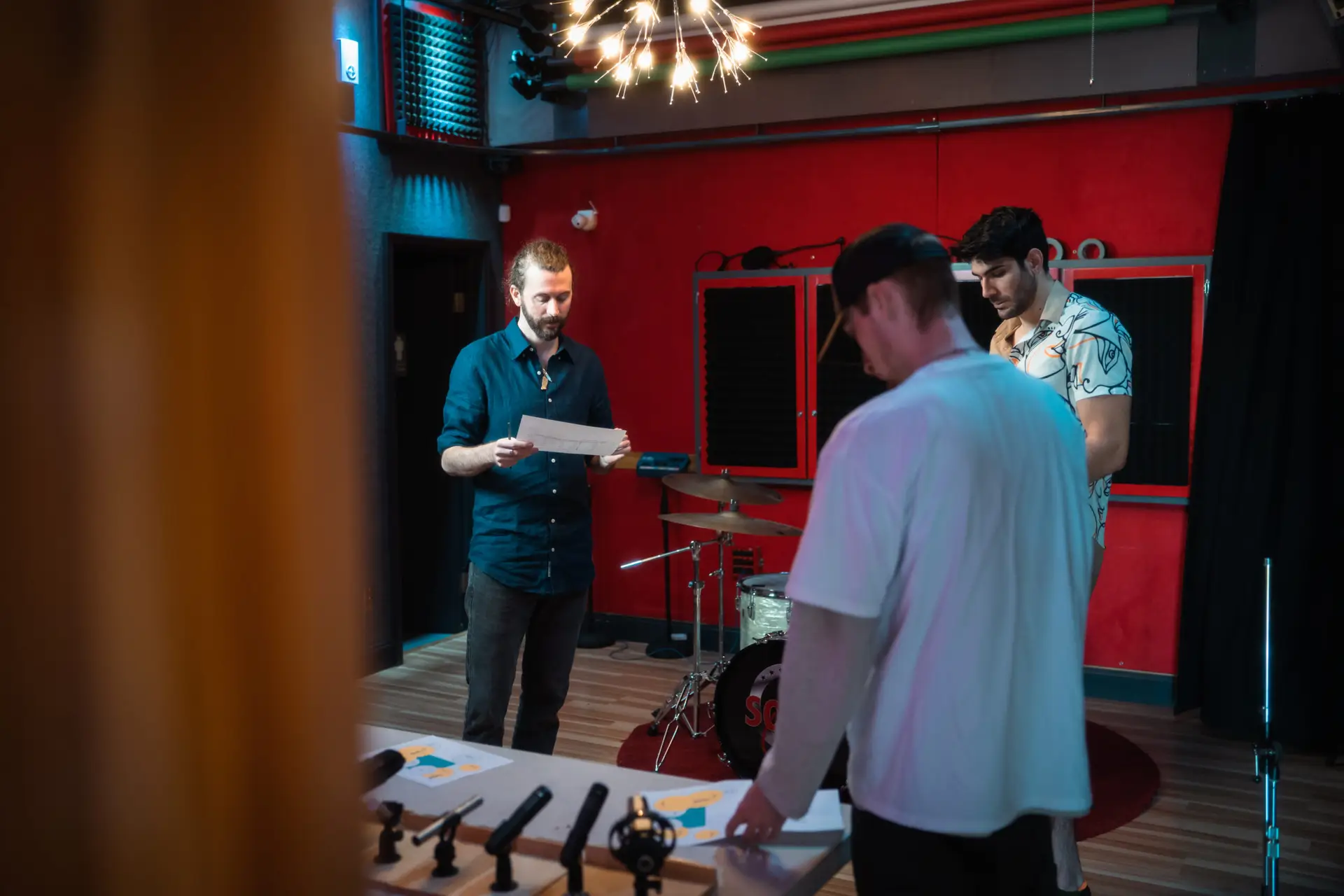 Three individuals in a recording studio reviewing documents with musical instruments in the background.