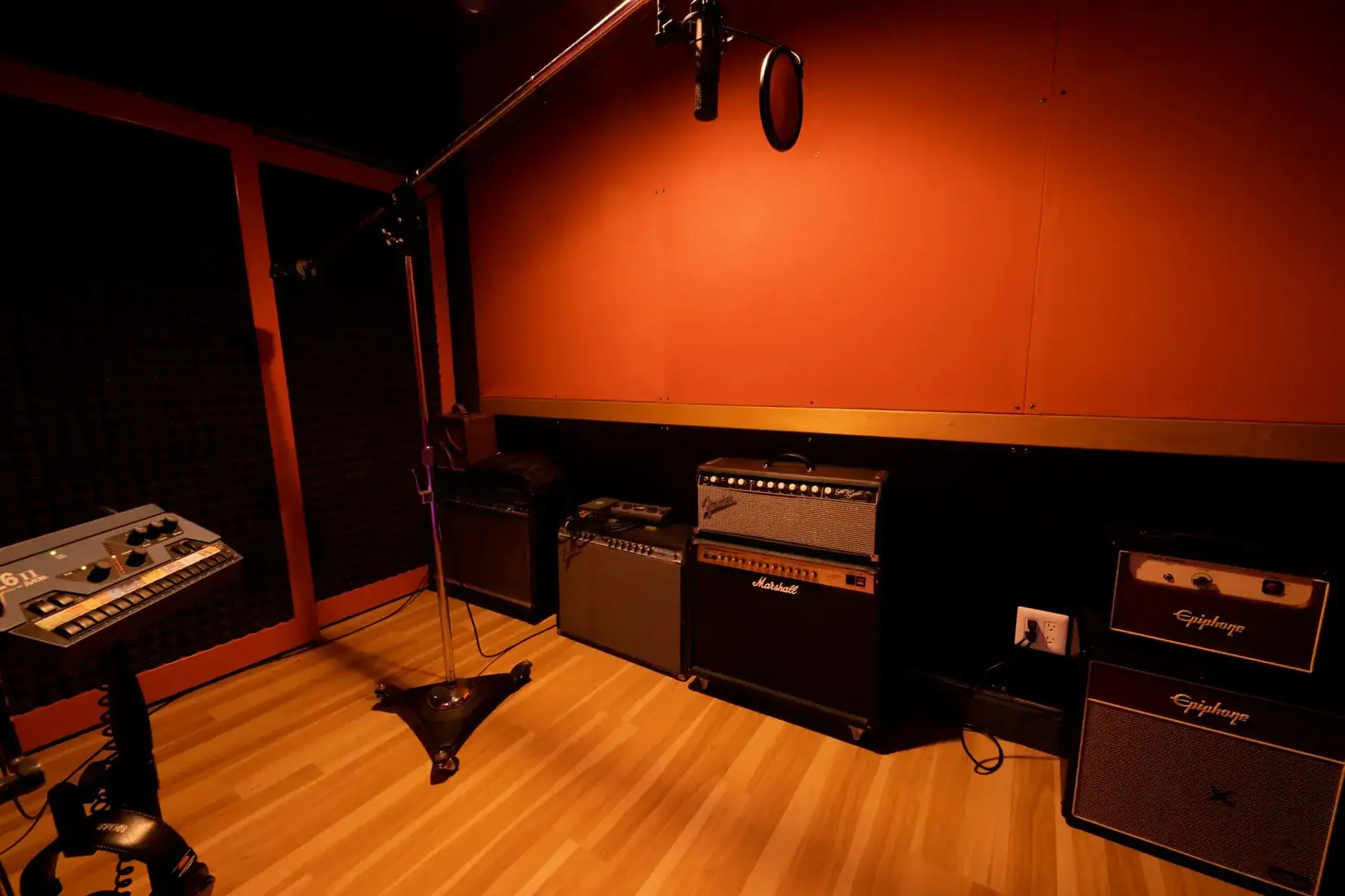 Recording studio featuring amplifiers and a microphone on a stand in a soundproof room.