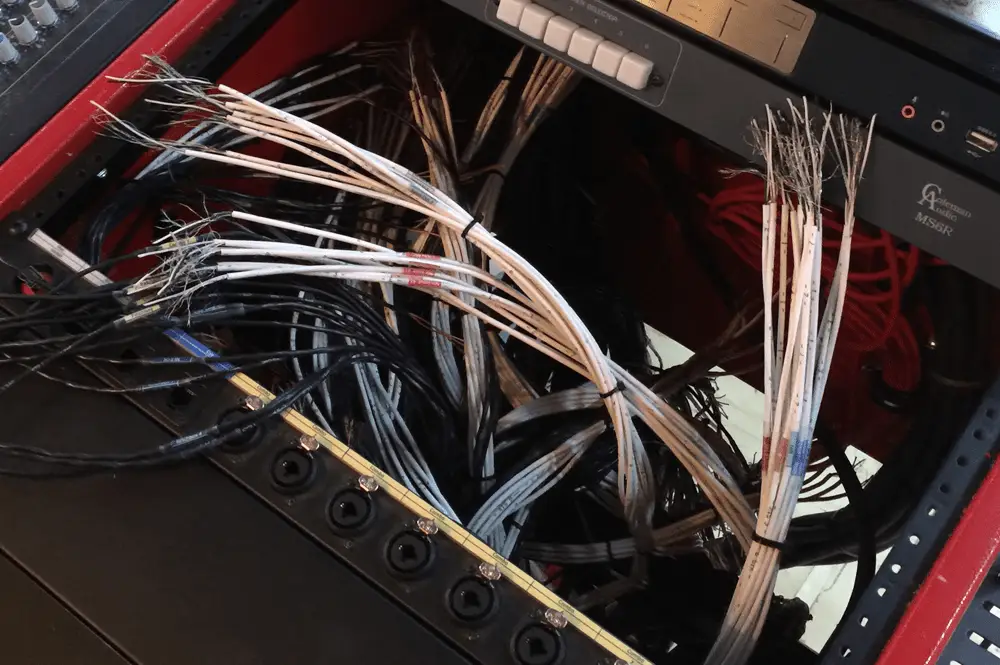 A collection of tangled network cables in a black equipment rack with various connectors.