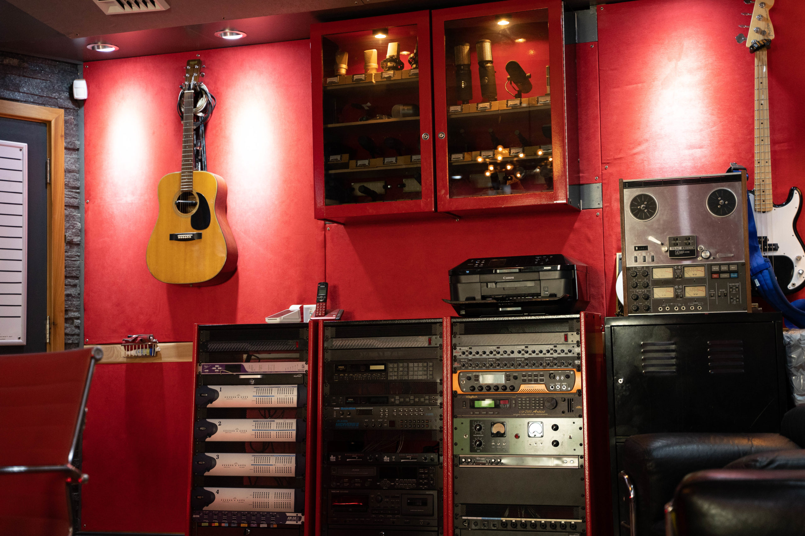 A red wall featuring an acoustic guitar, studio equipment, and a display cabinet in a recording studio.