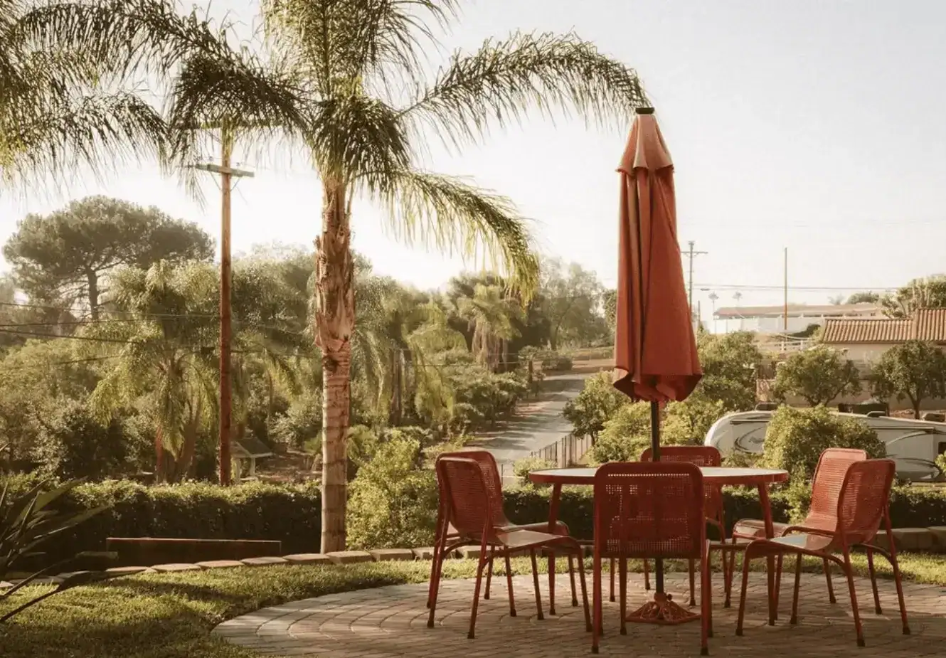 Red patio umbrella and chairs set on a stone patio with greenery in the background.