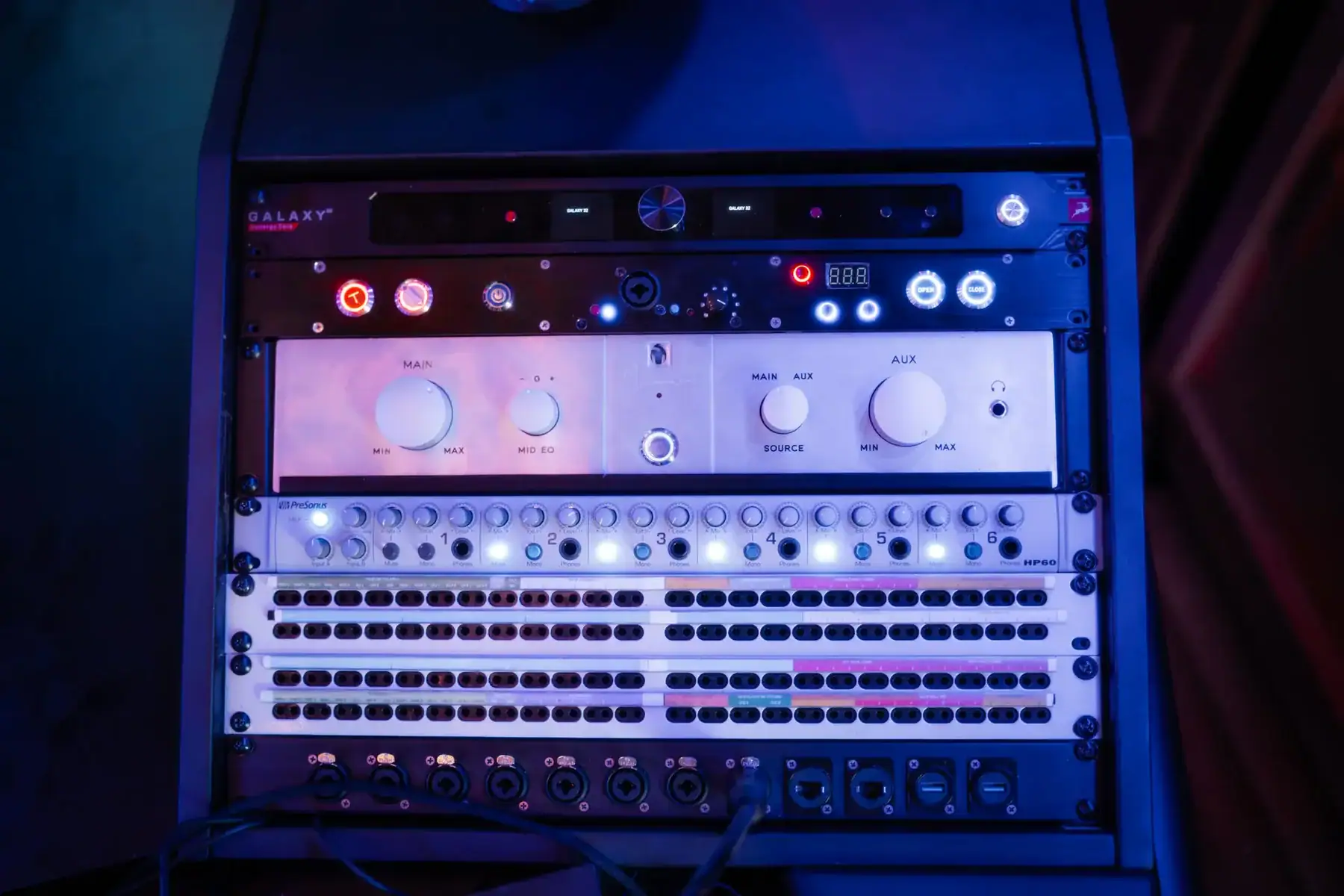 Audio mixing console featuring control knobs, buttons, and LED lights in a dark setting.