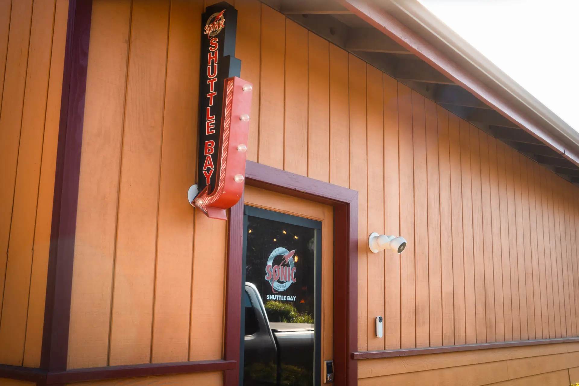 Sign for 'Shuttle Bay' with lights on the exterior of a building featuring wooden paneling.