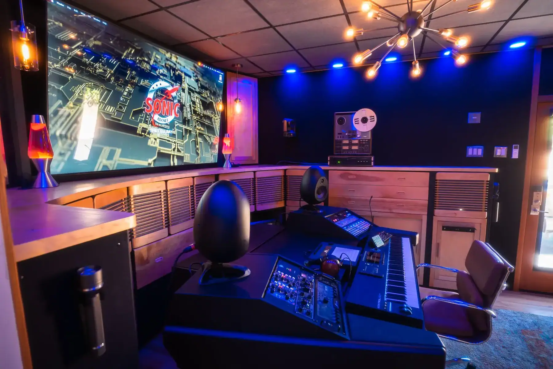 Interior view of a recording studio featuring a control desk and a large screen displaying Sonic logo.