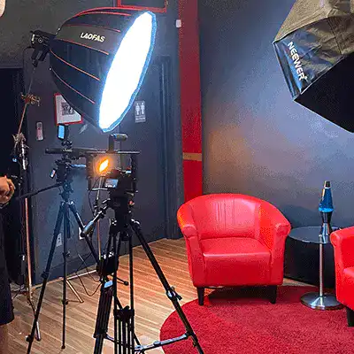 Music video lighting set at Sonic-Rocket: softbox lights, a camera on a tripod and a red armchair